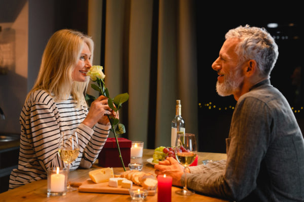 Happy middle-aged woman enjoying the rose fragrance during romantic dinner in the kitchen with her husband