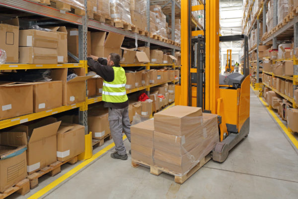 A warehouse worker picks a box off of a shelf in a fulfillment warehouse