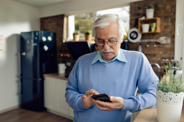 An older man texting on a phone in a kitchen