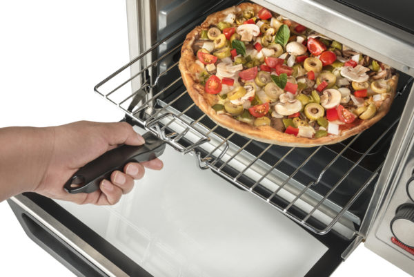 A hand removing a pizza from a toaster oven
