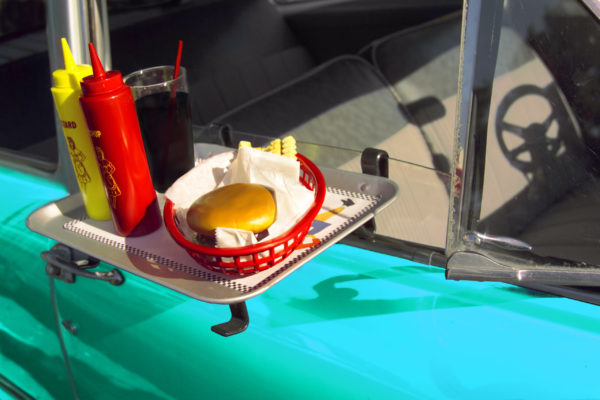 A fast food tray hangs on a classic car’s window at a drive-in