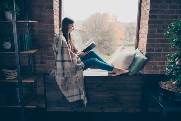 A woman reads in a reading nook with a blanket
