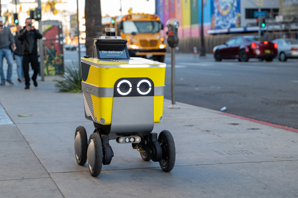 A delivery robot rolls down the sidewalk